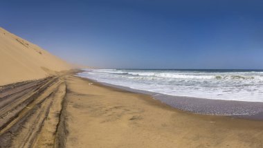 Naukluft çölünün kıyısındaki kum tepeleri ve Atlantik plajlı manzara, Walvis Körfezi, Namibya, Afrika 'daki parlak bahar ışığı altında çekildi.