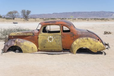 Naukluft çölündeki benzin istasyonunda paslanarak yıpranmış 40 'lı yılların araba enkazı Solitaire, Namibya, Afrika' da parlak bir bahar ışığı altında çekildi.