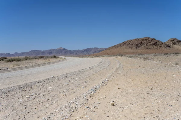 Naukluft Çölü 'ndeki Naukluftberge dağ sıraları, Susriem, Namibya, Afrika yakınlarındaki parlak bahar ışığı altında çekilen kıvrımlı çakıl yolu ve Naukluftberge dağ sırası.