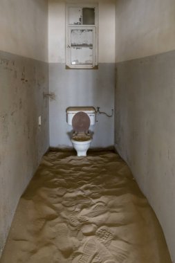 Çöl kumları, çöldeki hayalet kasabadaki terk edilmiş hastane binasının tuvaletinde su kabını yutuyor. Kolmanskop, Namibya, Afrika 'da parlak bahar ışığı altında vuruldu.