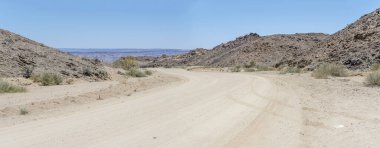 Çölde bükülen çakıl yolu ve Dolerite kaya popoları olan manzara, Hobas, Namibya, Afrika yakınlarındaki parlak bahar ışığı altında çekildi.