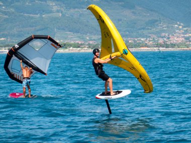 Fiumaretta di Ameglia, İtalya - 22 Ağustos 2024: insanoğlu ligurya denizinde kanat folyosu uyguluyor. Kanat folyosu, sörf ve uçurtmayı birleştiren dinamik bir su sporudur. İtici güç için elle tutulan şişme kanat kullanılır..