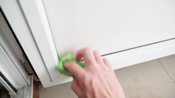 玄関のドアの白いプラスチック製の表面を洗う 手は洗剤 クローズアップとスポンジで白いプラスチック製のドアにゴム製の黒いシールをこすります 緑色のスポンジで湿らせた洗浄 — ストック動画