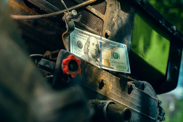 One hundred us dollars on a diesel engine of a minitractor close-up. Money and the agricultural industry. Maintenance and repair of agricultural machinery. Tractor breakdown and price