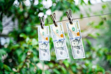 Yüz dolarlık banknotlar arka planda bulanık mandallarla asılı.