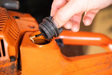 Bir el turuncu testere ile yakıt tankının kapağını açar. Benzin deposu. Yakından iki vuruşluk motor benzini. Elektrikli testereyi dolduruyorum.