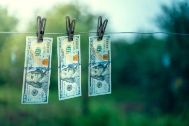 Yüz dolarlık banknotlar arka planda bulanık mandallarla asılı.