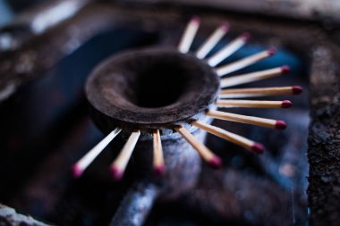 Jetlere kibrit sıkışmış eski kirli bir mutfak sobasının gaz ocağı. Gaz boru hattında gaz eksikliği ve mavi yakıt için yeni bir yer arayışı. Ağaç parçaları deliği kapatmış.