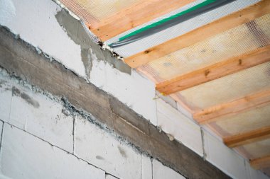 Havalandırmalı beton bir duvara kötü bir şekilde beton zırh kuşağı döküldü. Havalanmamış beton tuğlalardan yapılmış çıplak bir evin duvarları ve buhar bariyeriyle kaplı cam yünlü bir tavan..