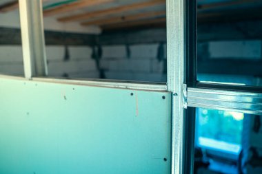 Çerçeveyi alçıpanla kaplama işleminin başlangıcı. Nemlendirmeye dayanıklı bir alçıpan tabakası, arka planda bulanıklığa karşı yakın plan çekimde metal bir profile vidalanmış.