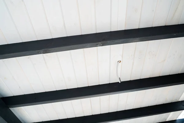 The ceiling of the street terrace is made of white wooden lining and black cross beams. Conducted wire in a corrugated pipe for lighting. Design solution in black and white colors
