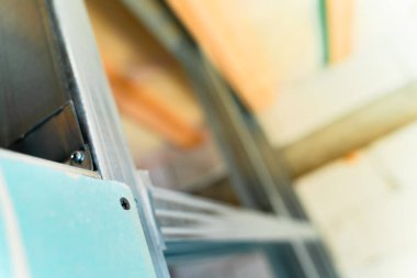 Çerçeveyi alçıpanla kaplama işleminin başlangıcı. Nemlendirmeye dayanıklı bir alçıpan tabakası, arka planda bulanıklığa karşı yakın plan çekimde metal bir profile vidalanmış.