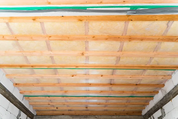Insulated ceiling of a private house with a wooden crate. The roof is insulated with glass wool and sheathed with a vapor barrier, bottom view