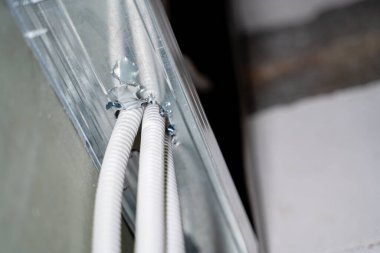 Koruyucu korkuluklu borudaki kablolar, alçı duvarın içindeki metal profil yoluyla delikten geçiyor. Çerçeve duvarının içindeki elektrik kabloları