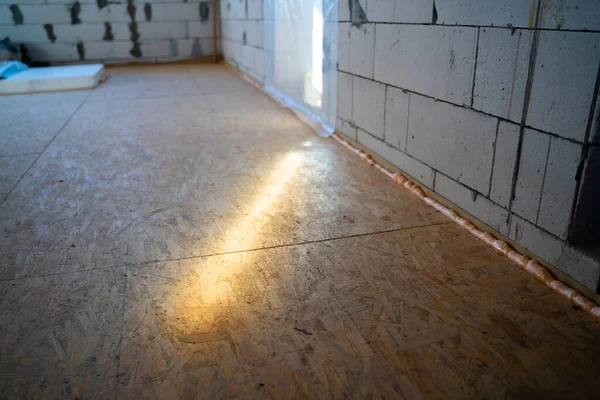 Light beam on an oriented strand board subfloor. The first leveling layer of OSB boards. Renovation process in a newly built private house. Thin long sun sunset beam at a construction site