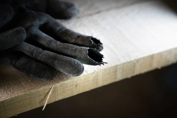 Black construction glove with rubbed fingers close-up. Holeful work gloves at a construction site on wooden scaffolding. Poor quality protective gloves torn at the fingers. Worn Builder\'s Equipment