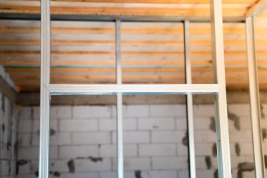 Alçıpan paneller için yapılmış metal çerçeve. Odanın duvarları için metal bir profil çerçevesi. Tamiri olmayan yeni yapılmış özel bir evin çıplak duvarları.