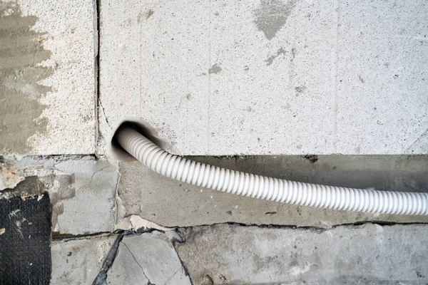 The wire in a protective plastic corrugated pipe is laid through the wall through a hole in the aerated concrete brick. Conducting electricity to the house. Drilled hole in gas block