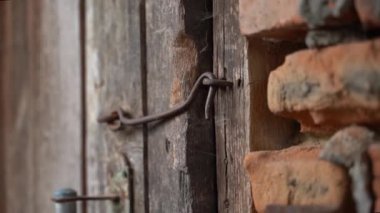 An old wooden door in a brick wall is locked with a vintage iron hook close-up. Smooth parallax. High quality FullHD footage
