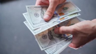 Hands counting a stack of one hundred dollar bills close-up on a blurred background. Man holds out a large sum of money. High quality 4k footage