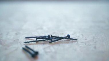 Long black self-tapping screws lie on an oriented strand board close-up against a blurred background. Smooth camera parallax. High quality FullHD footage