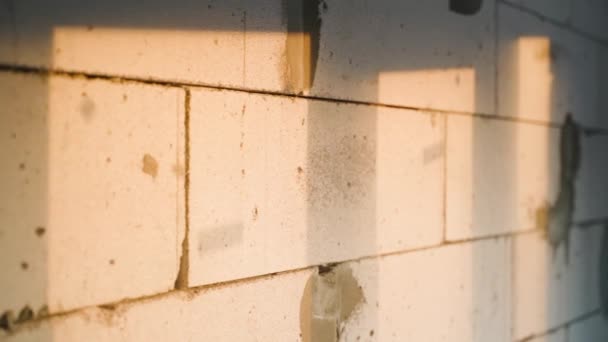用落日的温暖落日的余晖照射在裸露的混凝土墙面上 晚上在建筑工地的窗前有阴影 镜头沿着充气混凝土挡土墙平稳地移动 — 图库视频影像