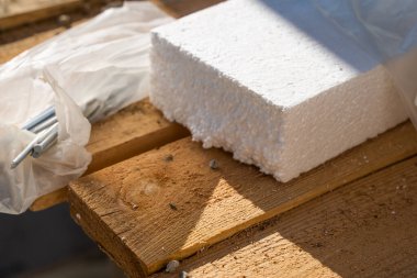 Thick white polystyrene foam for home insulation on wooden boards. Long thick nails for attaching insulation to walls