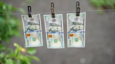 Clothespins hold three paper one hundred dollar bills close-up on a blurred background. Smooth parallax camera movement. High quality FullHD footage