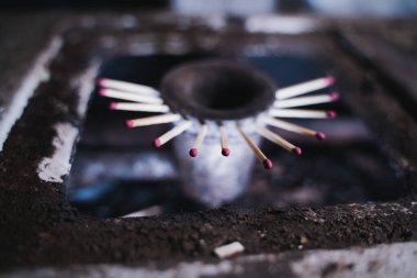 Jetlere kibrit sıkışmış eski kirli bir mutfak sobasının gaz ocağı. Gaz boru hattında gaz eksikliği ve mavi yakıt için yeni bir yer arayışı. Ağaç parçaları deliği kapatmış.