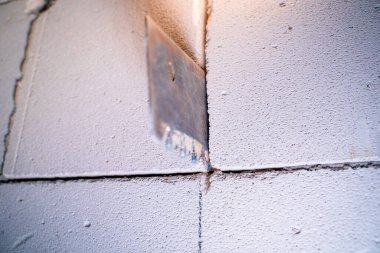 A hacksaw for aerated concrete sticks out of a wall of aerated concrete bricks close-up on a blurred background. Cutting a doorway in a gas block wall, handmade