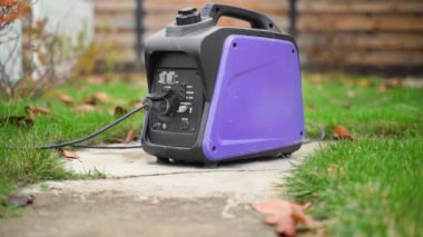 A small gasoline inverter generator with a wire connected to a socket works on the street close-up. Purple power generator with a plastic case. Alternative power source in case of blackout. High