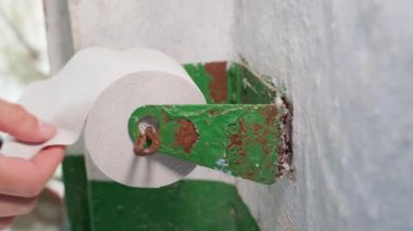 The hand pulls toilet paper from the holder close-up. Facilities in the outdoor rural toilet. Single ply cheap toilet paper roll. High quality 4k footage