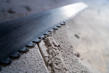 Aerated concrete hacksaw lies on an aerated concrete brick with scraps, top view. Hand saw on a gas block close-up. Adjusting the size of building materials manually