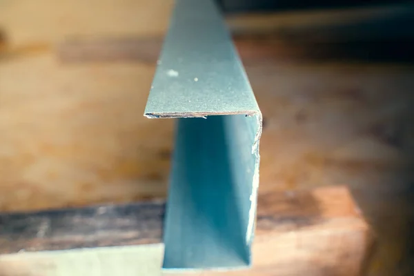Close-up of a fresh cut of a metal U profile against a blurred background. Sharp edges of the metal profile after the grinder