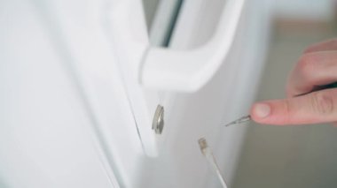 Two hands are trying to break the door lock with master keys close-up, top view. A man inserts screwdrivers into the lock of a white plastic door in order to break into and enter the house. High