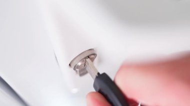 Bir el anahtarı beyaz plastik bir kapının anahtar deliğinde çevirir ve anahtarı kilitten çıkarır. Yüksek kaliteli FullHD görüntüler
