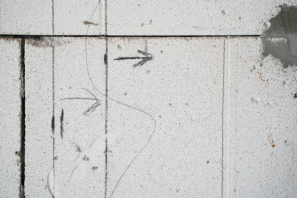 Crossed lines drawn in pencil on a bare aerated concrete wall. Designation of future walls with lines and arrows on the gas block, house layout