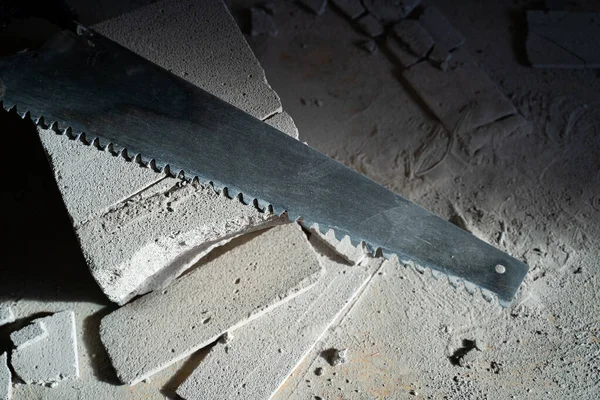 Aerated concrete hacksaw lies on an aerated concrete brick with scraps, top view. Hand saw on a gas block close-up. Adjusting the size of building materials manually
