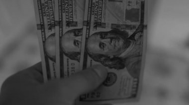 Bir el karanlıkta 300 dolar tutar, bulanık bir arka planda yakın plan. Yüz dolarlık banknotları olan siyah beyaz bir video. Yüksek kaliteli FullHD görüntüler