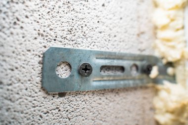 Havalandırmalı beton tuğlalardan oluşan bir duvara pencere dikti. Siyah kendini beceren vida havalandırmalı betona vidalanmış.