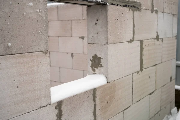 A hole in the wall of aerated concrete bricks for a square window. Snow on a construction site in spring