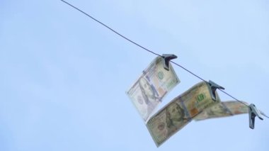 Yüz dolarlık banknotlar çamaşır mandallarıyla rüzgarda gökyüzüne karşı çırpınıyor. Yüksek kaliteli FullHD görüntüler
