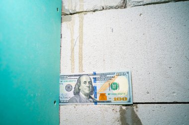 Alçıdan bir duvar ve havalandırılmış beton bloğun kesiştiği yerden 100 dolarlık banknotun yakın plan çekimi. Neme dayanıklı alçıpan ve gaz bloğu