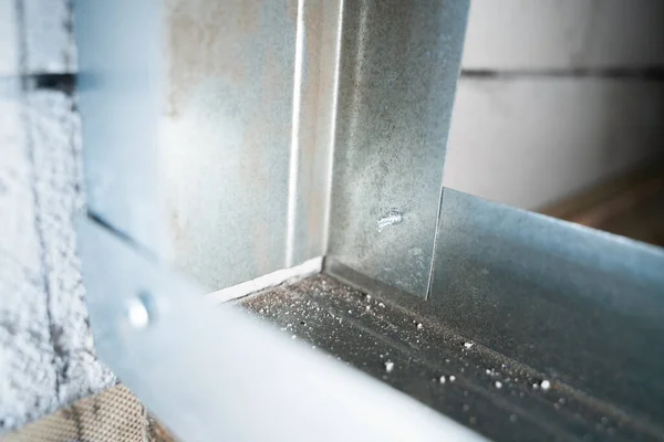 Two metal profiles are connected at a right angle with a stainless steel self-tapping screw with a drill close-up. Assembling the frame for drywall from a metal profile