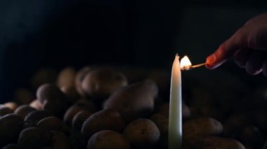 Bir el bodrumda ince beyaz bir mum yakar. Tahta kibrit, karanlıkta patatesin içindeki bir mumun fitilini tutuşturur. Yüksek kalite 4k görüntü