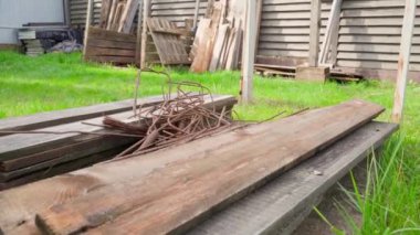 Eski tahtalar ve paslı metal çubuklar sokaktaki yeşil çimlerde uzanıyor, düzgün kamera hareketleri. Yüksek kaliteli FullHD görüntüler