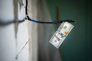 Yüz dolarlık banknot, arka planda bulanık bir zemine bağlı beton bir duvara bağlı bir elektrik kablosuna asılı. Elektrik hizmetleri için ödeme. Elektrik için yükselen fiyatlar