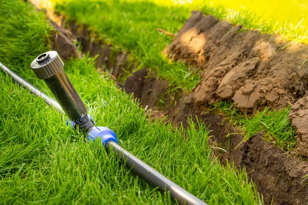 Bitmiş çimenlikte geri çekilebilir fıskiyeyle kendi kendine sulama sistemi. Su borularını sulama için çimlerin altına sprey ile döşüyorlar..