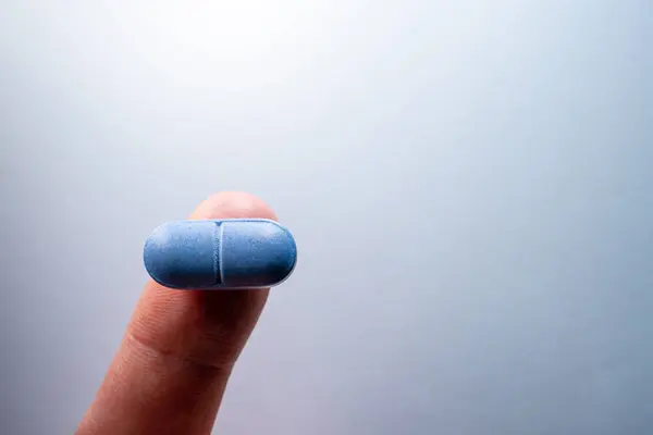 A finger holds a blue oblong pill close-up. Decided to take the blue pill