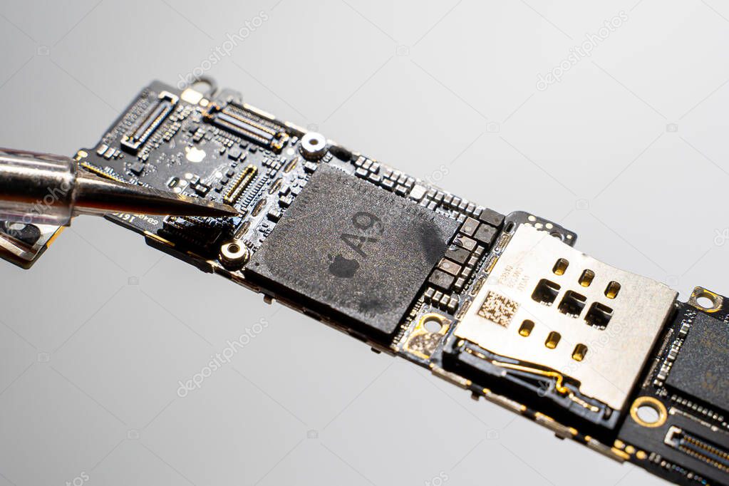 Kyiv, Ukraine - August 25, 2023: Motherboard with Apple A9 processor and a screwdriver, close-up. Board with iPhone SE chip in service